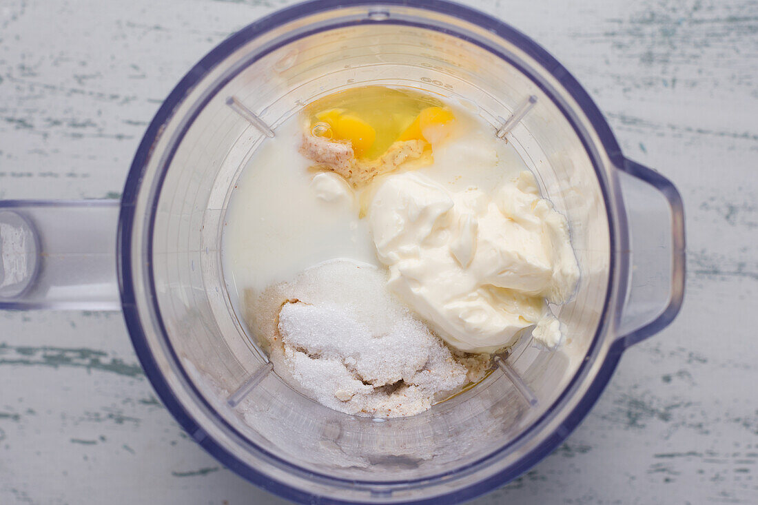 Draufsicht auf Produkte für Keto-Crepes mit Ei und Frischkäse mit Erythrit-Süßstoff im Mixer auf dem Tisch in der Küche