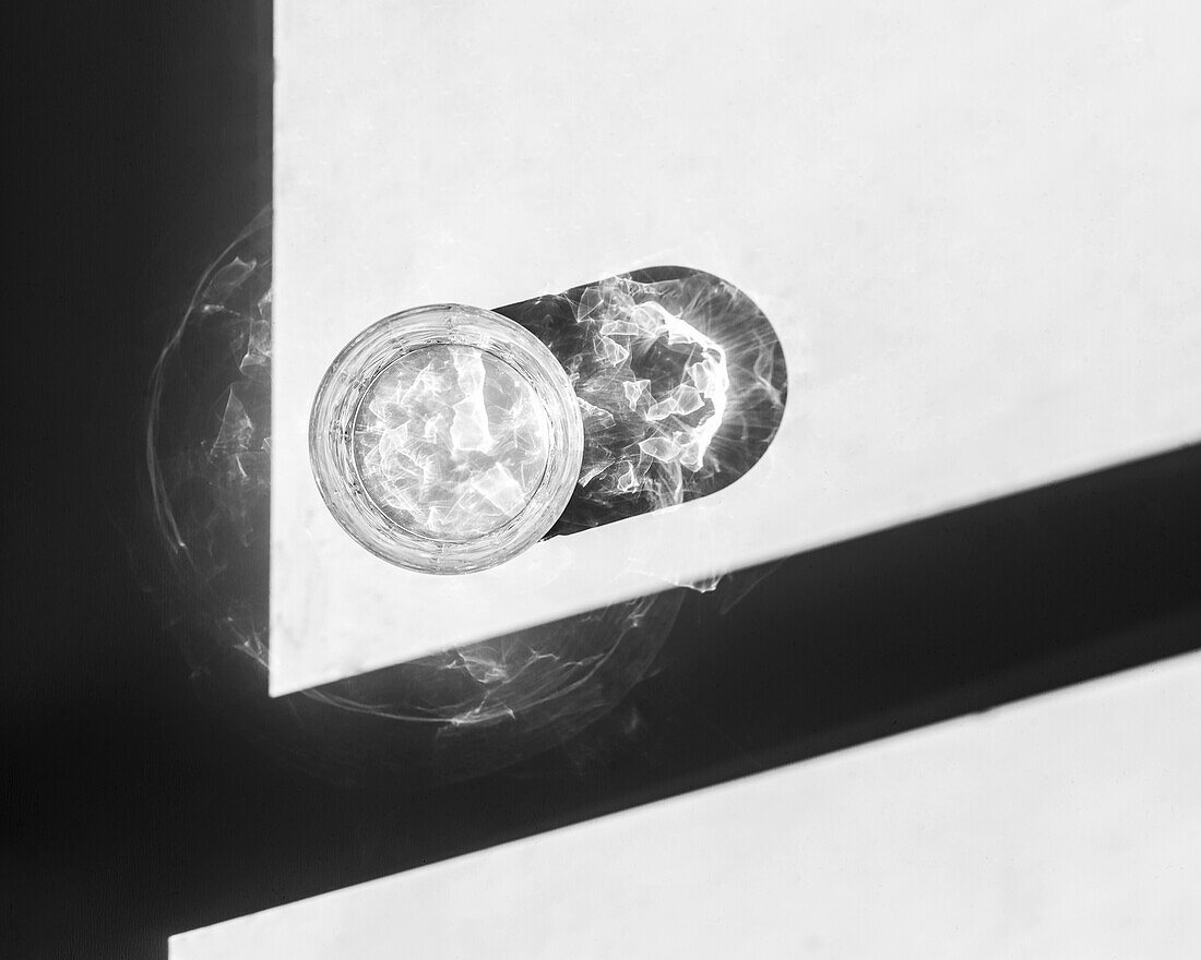 From above empty lowball glass placed on white table near shadow and reflecting bright sunlight in daytime