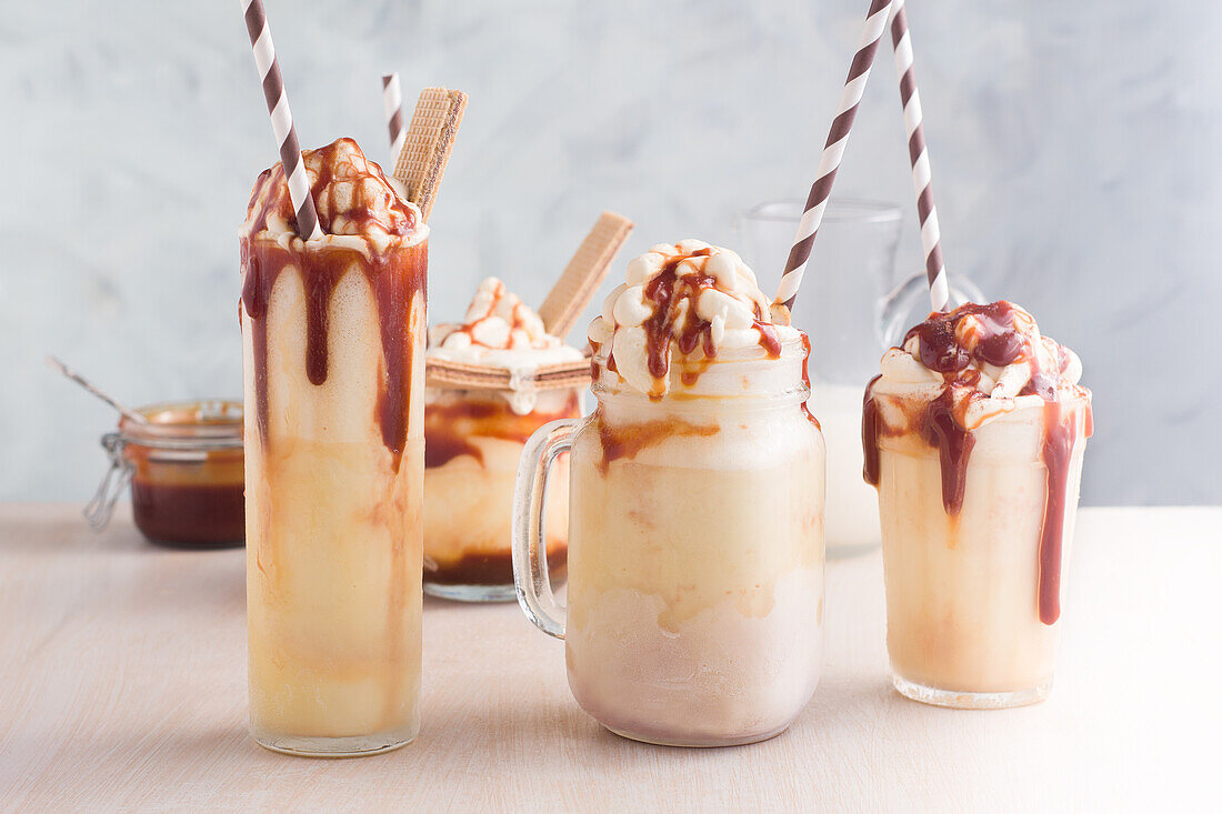 Verschiedene Gläser mit süßem Karamellmilchshake mit Vanilleeis und Waffelkeksen auf einem Tisch