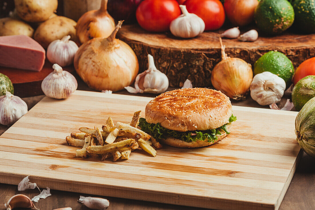 Appetitliche Hamburger mit Gemüse auf Holzbrett mit Pommes frites in Küche