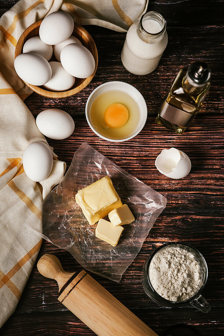 Top view of various ingredients for baking near cooking tools placed on wooden table in kitchen