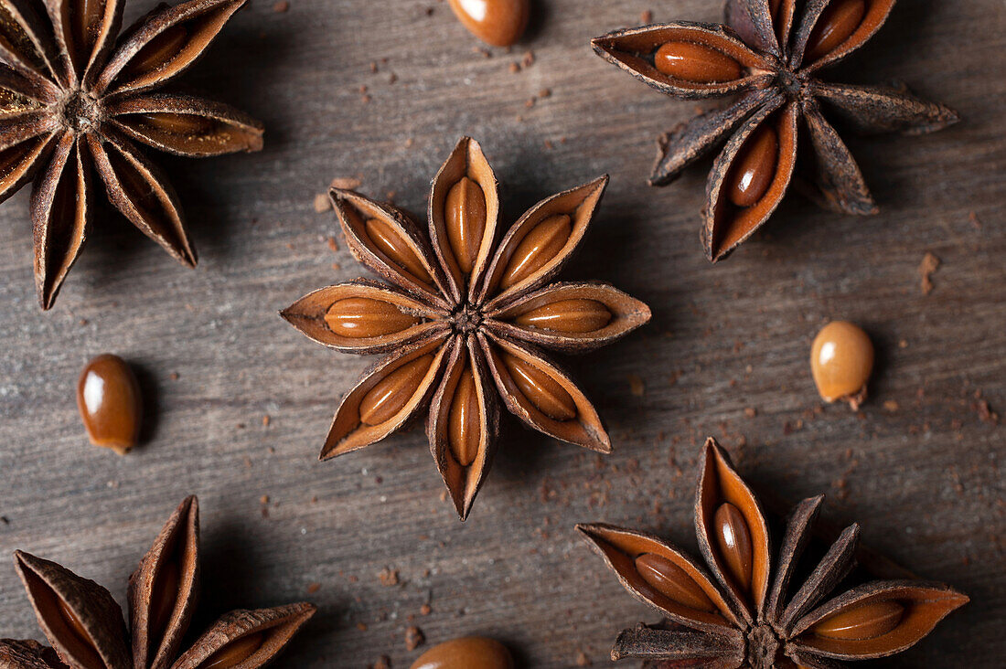 Closeup of aromatic dried anise stars with seeds scattered on rustic wooden table for gastronomy concept background