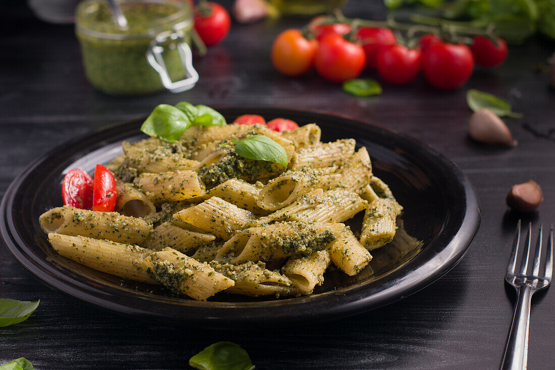 From above of plate with delicious pasta with green pesto sauce and tomatoes served on black wooden table