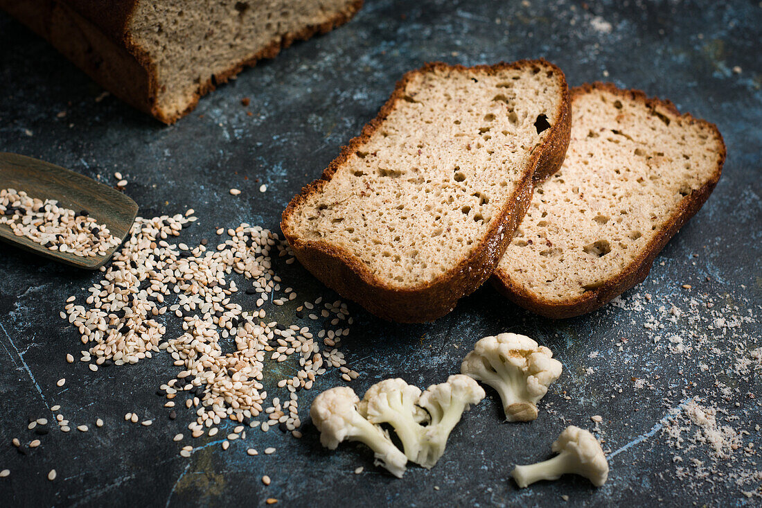 Ansicht von oben Laib und Scheiben von gesundem Brot auf Tisch mit Löffel in verstreuten Sesamsamen in heller Küche