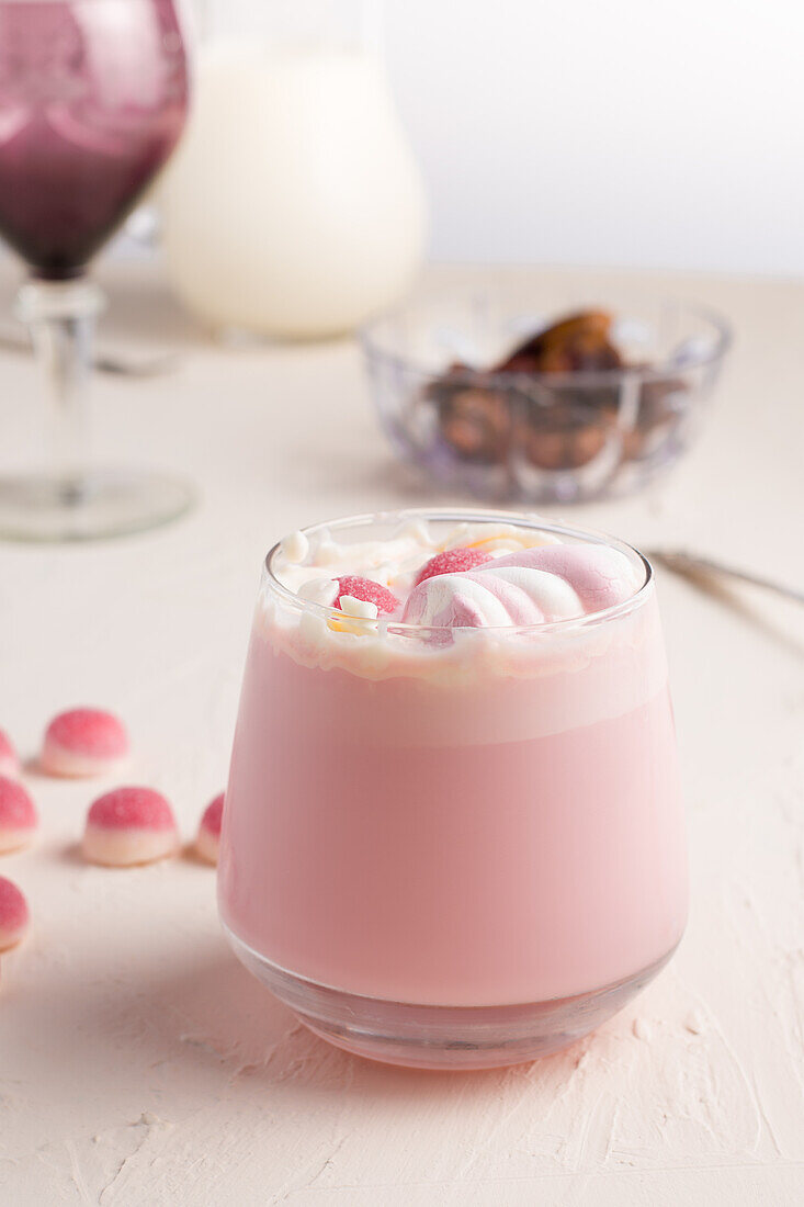 Glas mit süßer heißer weißer Schokolade mit rosa Geleebonbons und Marshmallow auf weißem Tisch