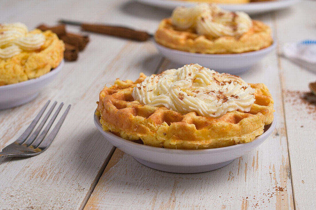 Frisch gebackene hausgemachte Kürbis-Käse-Waffeln mit Zuckerguss auf einem Holztisch mit Zimtstangen in einer hellen Küche