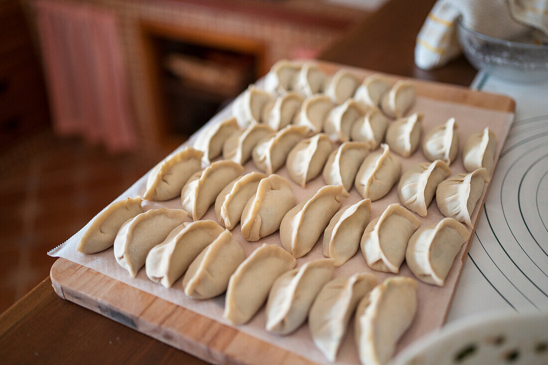 Von oben gesehen rohe traditionelle Jiaozi-Klöße, die auf einem hölzernen Schneidebrett in der Küche serviert werden