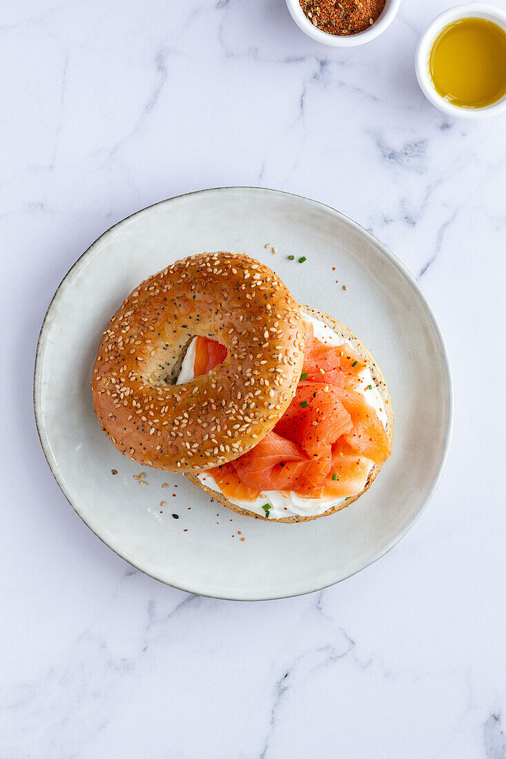 Von oben frischer Bagel mit Käse und Lachs auf einem Teller, serviert auf einem Tisch mit einer Tasse heißem Kaffee in einer hellen Küche