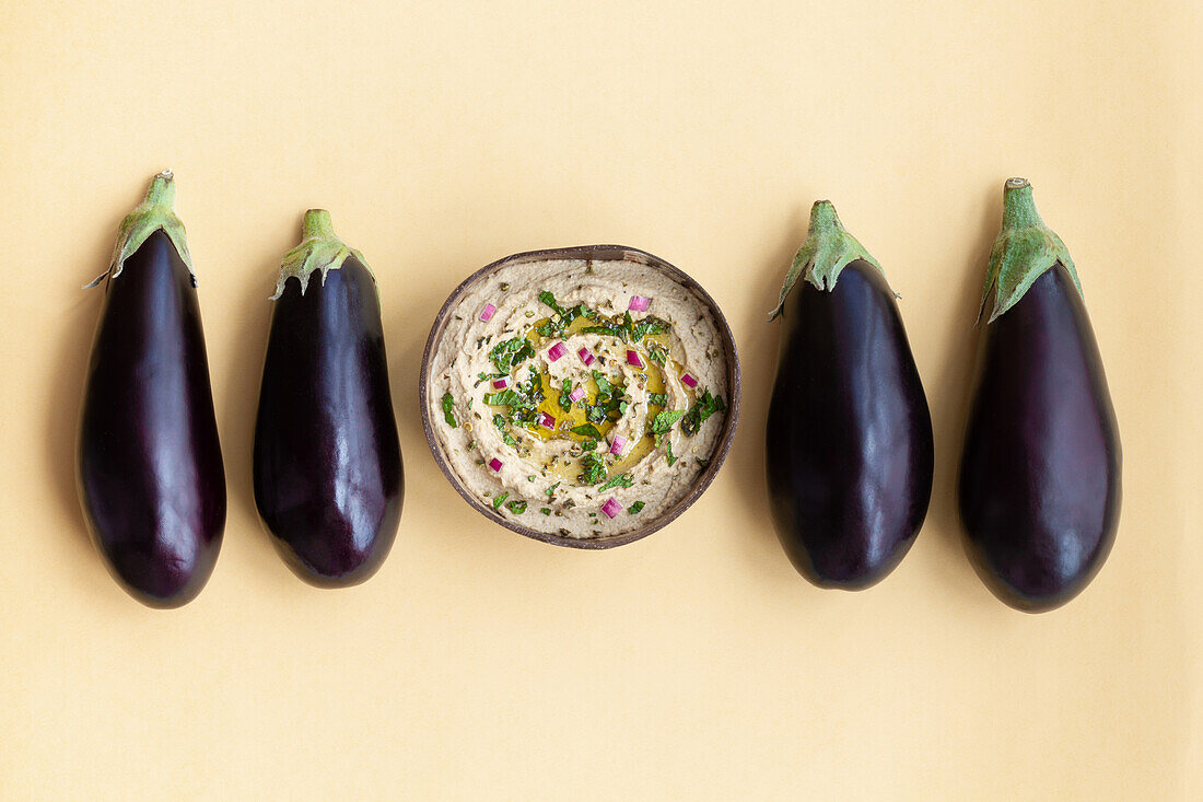 Draufsicht auf frische, reife Auberginen, die auf einem beigen Tisch mit einer Schüssel des appetitlichen traditionellen Gerichts Baba ghanoush platziert sind