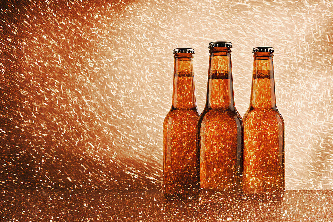Glass bottle of cold beer surrounded by sparkling lights on bright background
