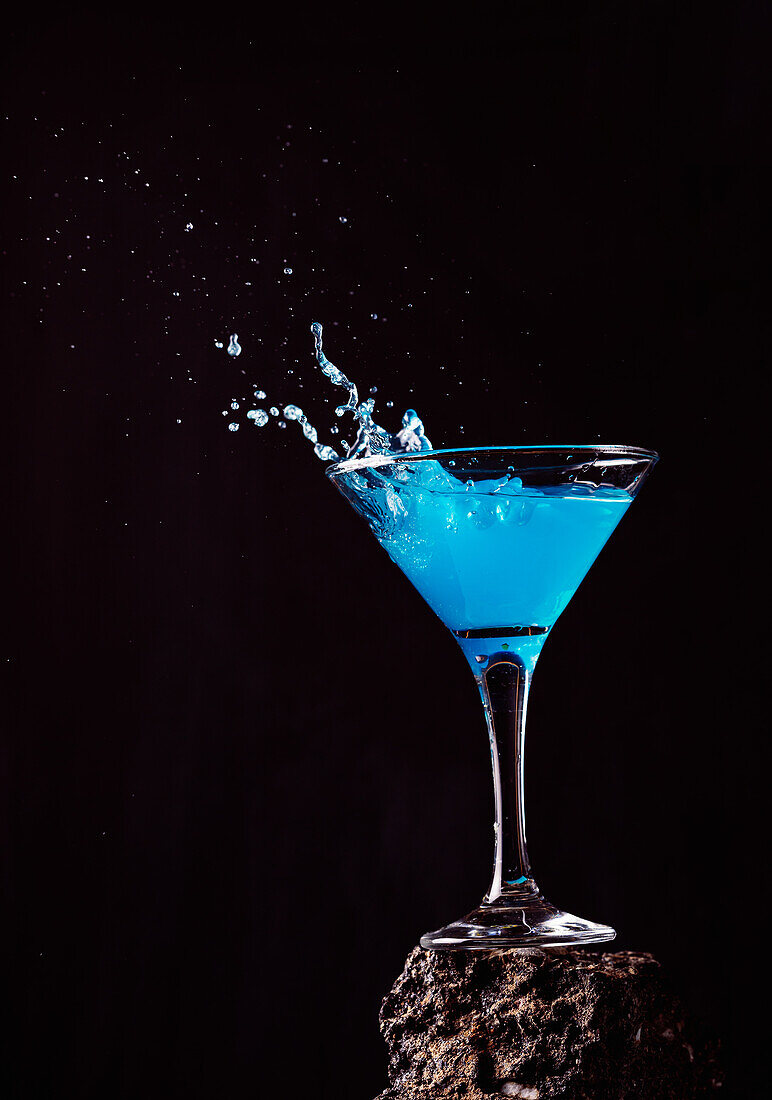 Blaue-Lagune-Cocktail in elegantem Kristallglas auf rauer Oberfläche vor schwarzem Hintergrund