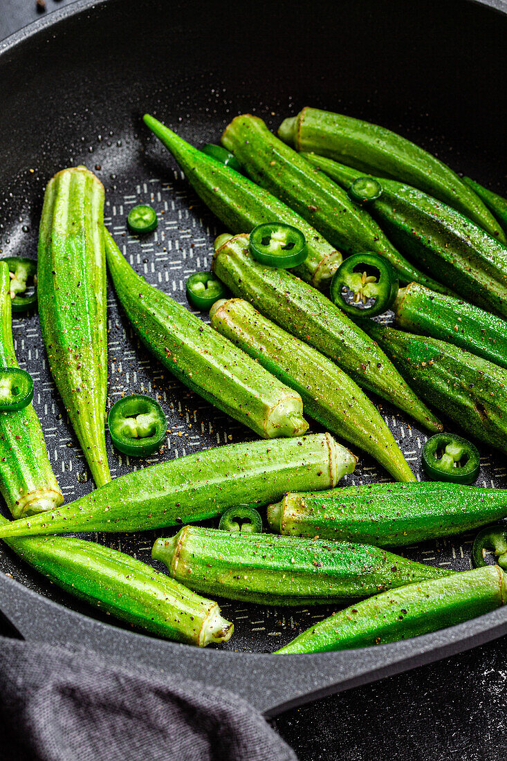 Von oben aufgerissene frische Okra in der Pfanne mit grünem Pfeffer auf dunklem Hintergrund