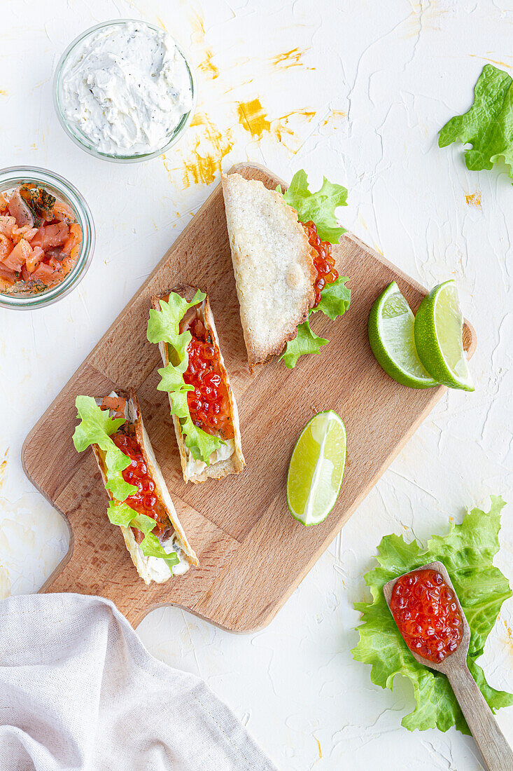 Kleine leckere Tacos mit rotem Kaviar und grünem Salat, serviert auf einem hölzernen Schneidebrett auf dem Tisch