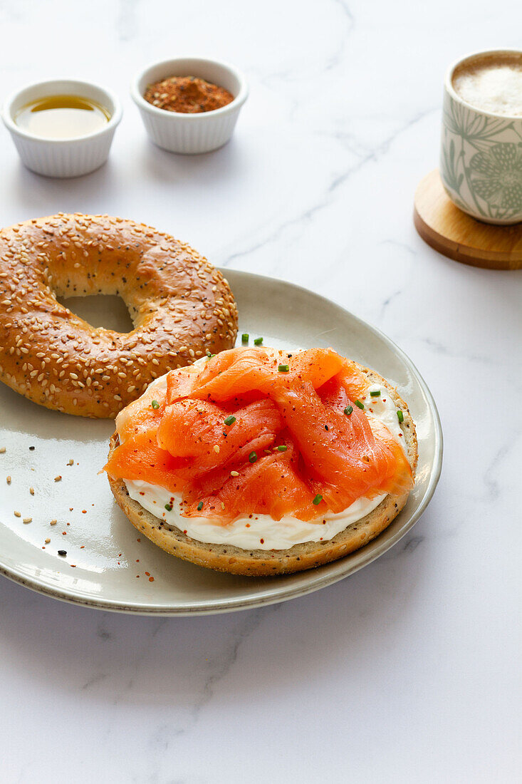 Frischer Bagel mit Käse und Lachs auf einem Teller, serviert auf einem Tisch mit einer Tasse heißem Kaffee in einer hellen Küche