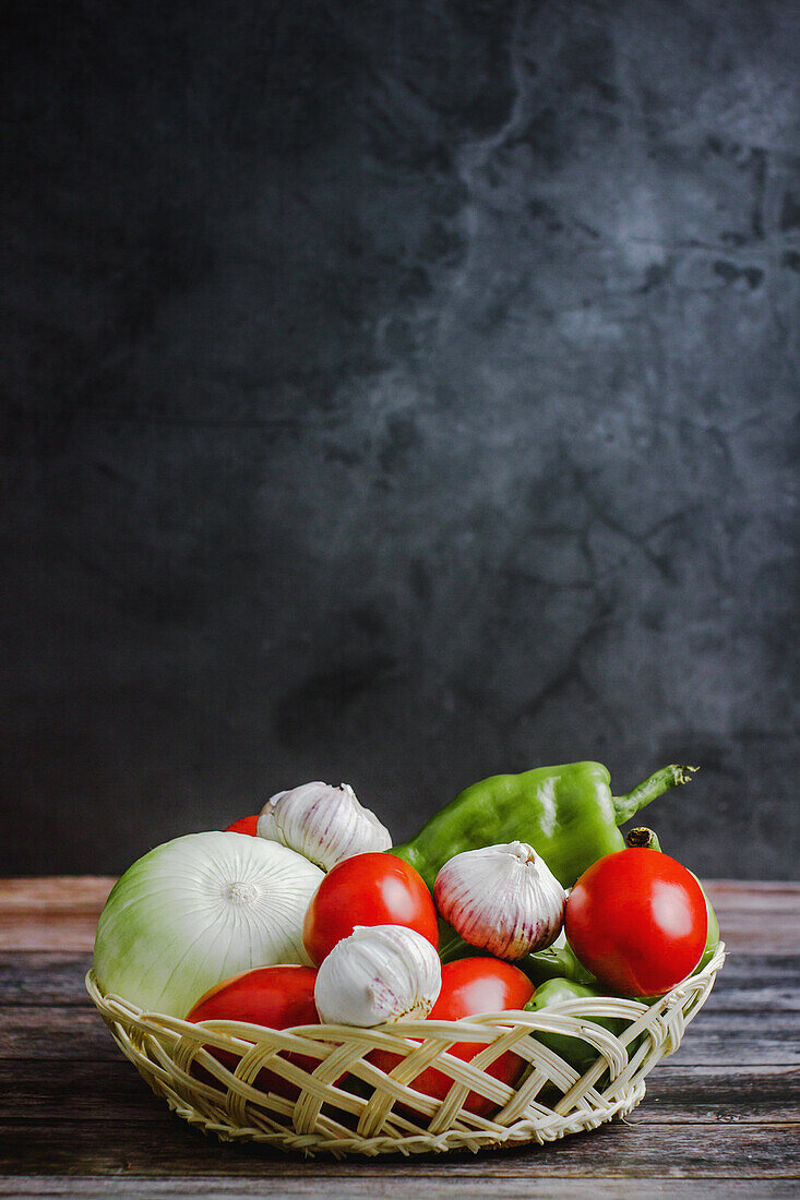 Frische reife Tomaten neben Paprika und Knoblauch in einer Schüssel auf einem Holztisch zu Hause