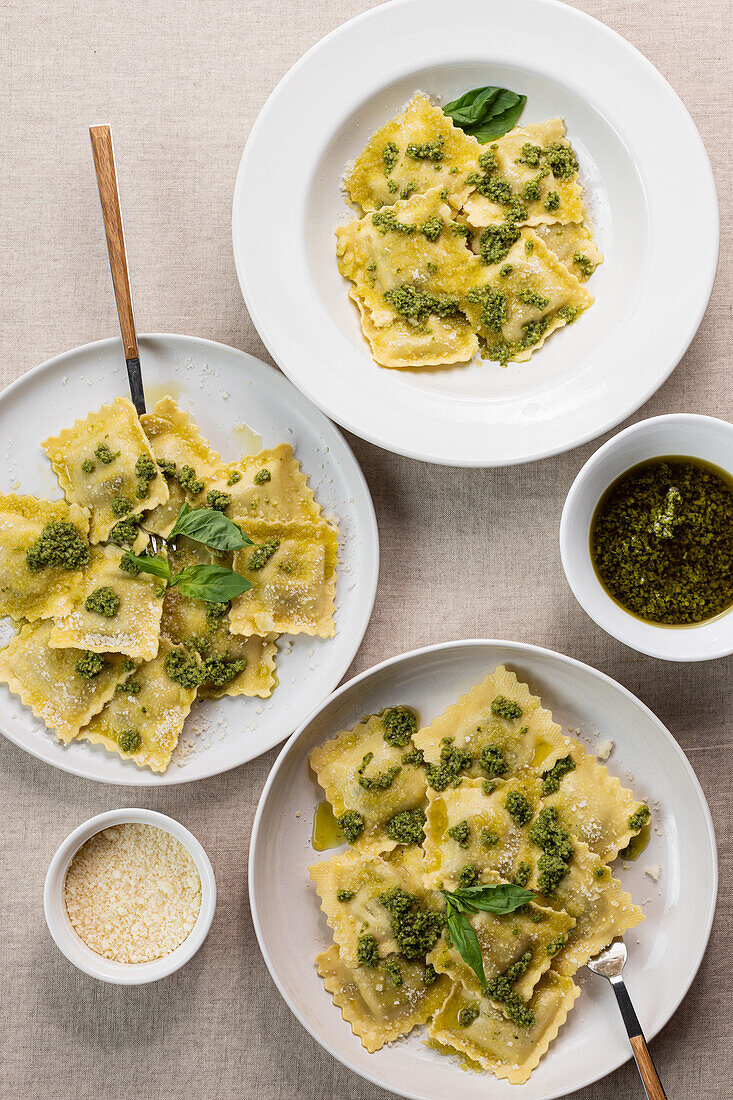 Draufsicht auf appetitlich gekochte Ravioli mit grüner Soße und Kräutern auf weißen Tellern mit Gabeln auf dem Tisch