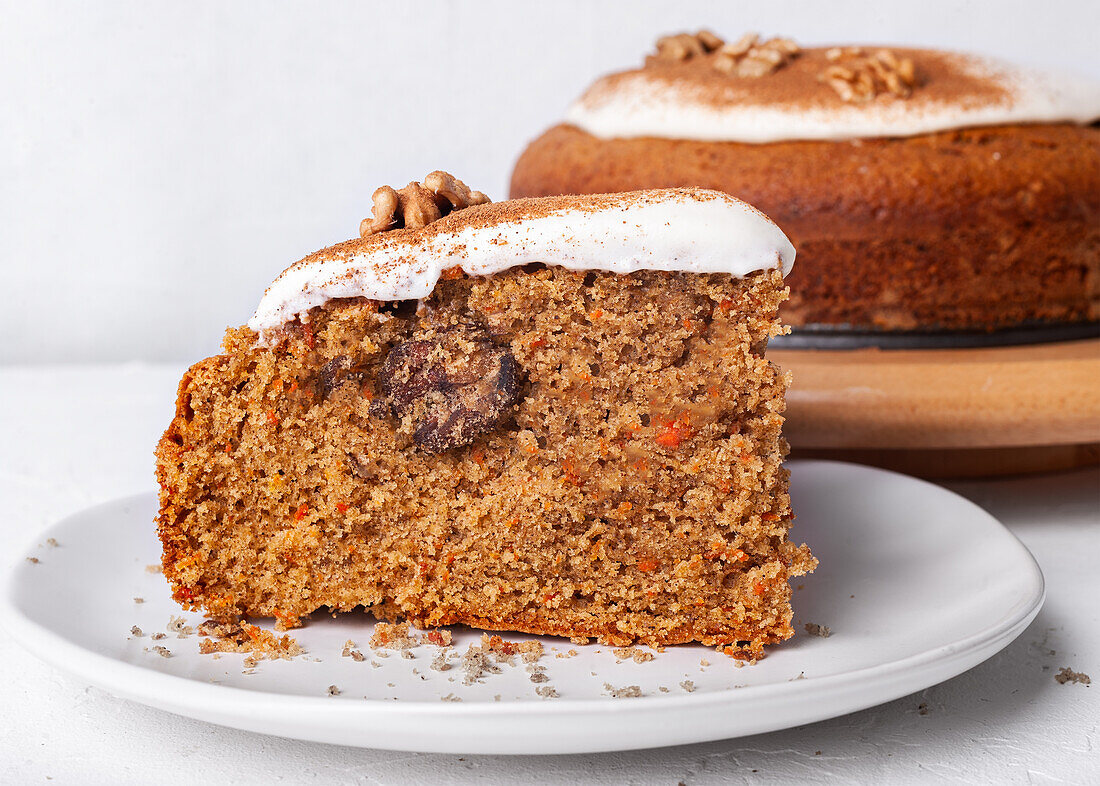 Tasty carrot cake piece with walnut and cinnamon powder on icing sugar glaze on light background