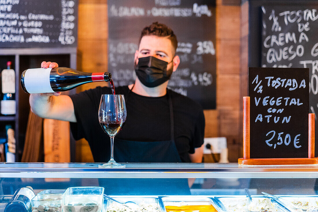 Anonymer Barkeeper gießt Wein aus einer Flasche in ein Glas am Tresen eines Restaurants mit vielen Schildern