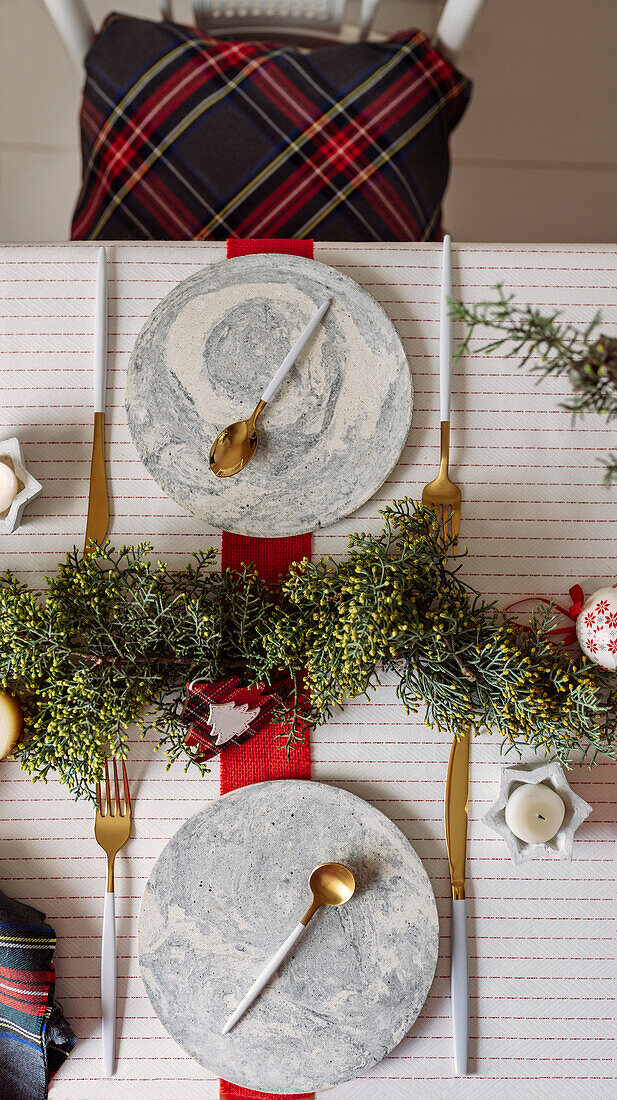 Von oben auf einen weihnachtlich gedeckten Tisch mit Kranzdekoration, rot und weiß, mit goldenem Besteck und Kerzen