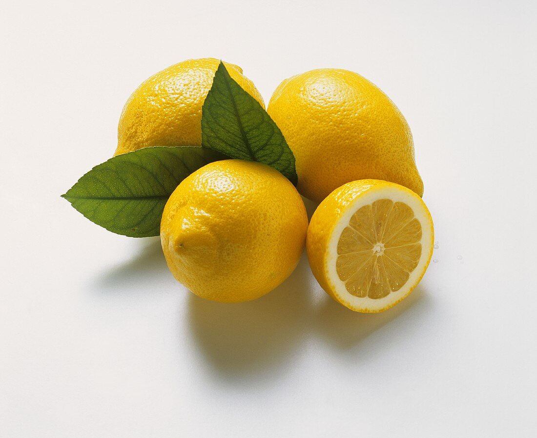 Drei Zitronen mit zwei Blättern und eine Zitronenhälfte