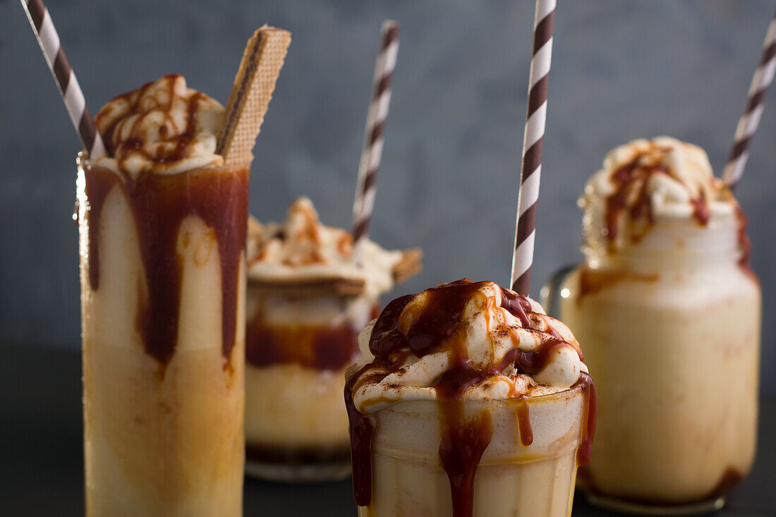 Verschiedene Gläser mit süßem Karamellmilchshake mit Vanilleeis und Waffelkeksen auf einem Tisch