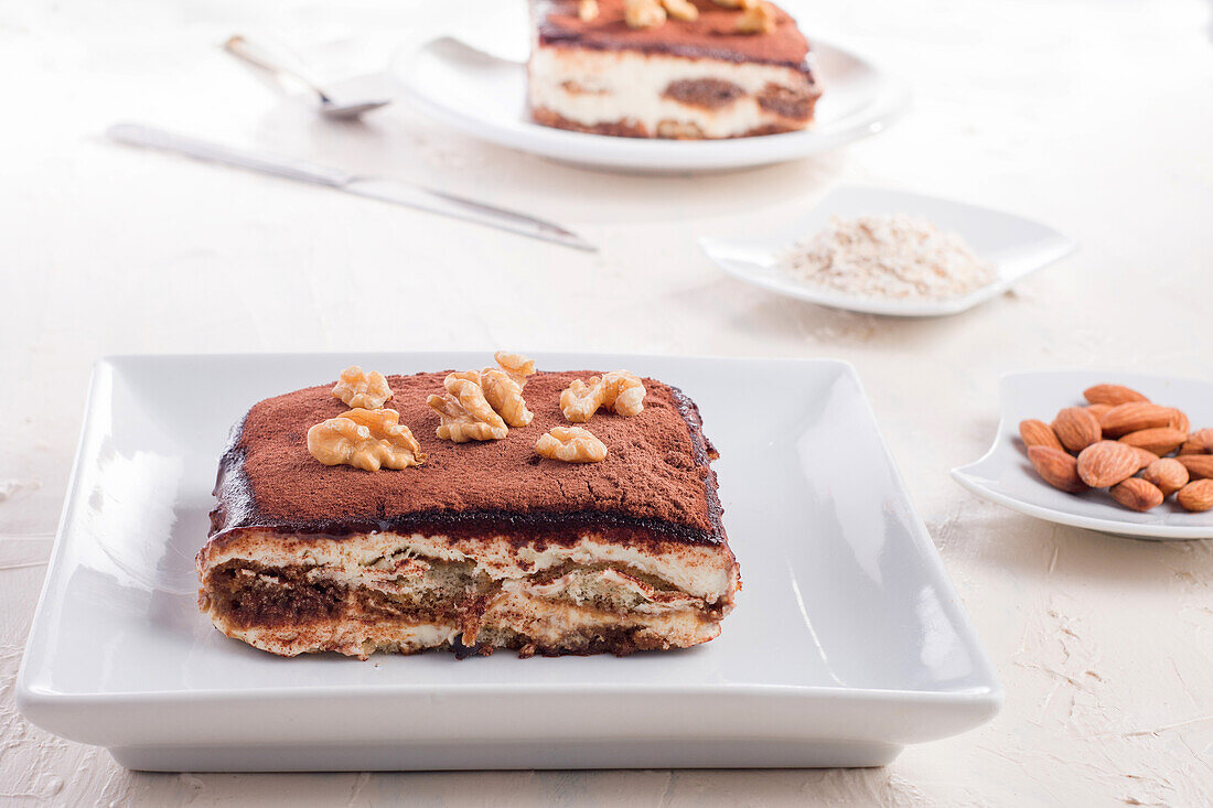 Hoher Blickwinkel auf köstliches Tiramisu-Dessert mit Walnüssen garniert auf einem weißen Tisch