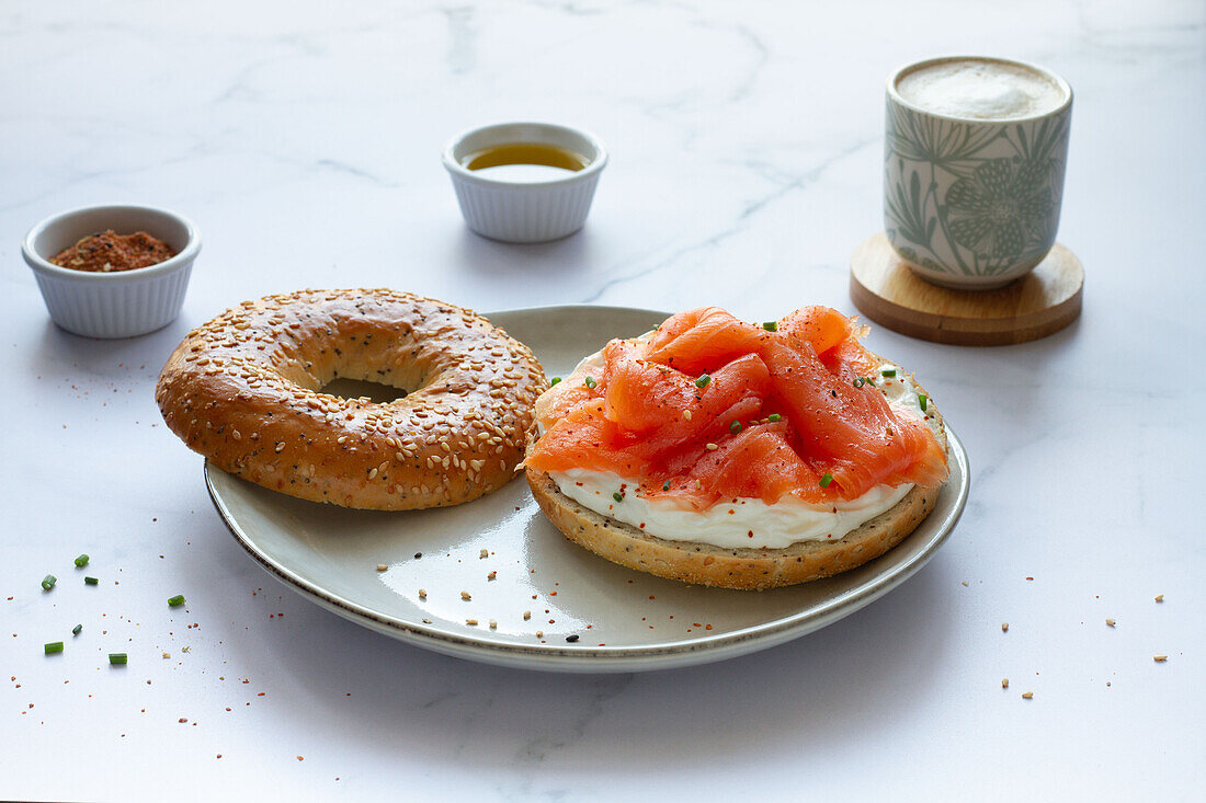 Frischer Bagel mit Käse und Lachs auf einem Teller, serviert auf einem Tisch mit einer Tasse heißem Kaffee in einer hellen Küche