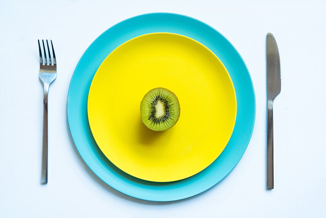 Blick von oben auf die Hälfte einer frischen, reifen, saftigen Kiwi, die auf gelben und blauen Tellern auf einer weißen Fläche liegt