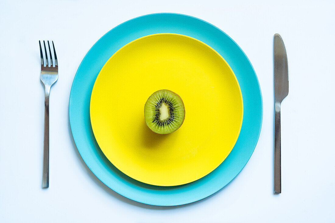 From above of half of fresh ripe juicy kiwi placed on yellow and blue plates on white surface