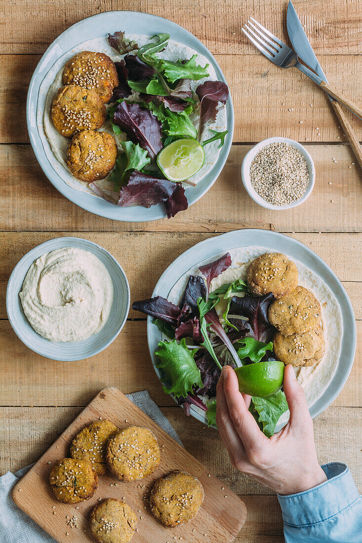 Teller mit frischem Salat und Süßkartoffel-Falafel neben Soße und Sesam auf Holztisch