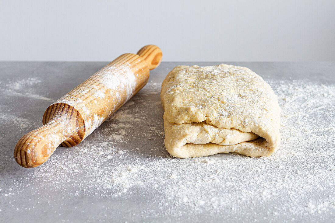 Wooden rolling pin near soft dough with flour during cooking process in countertop