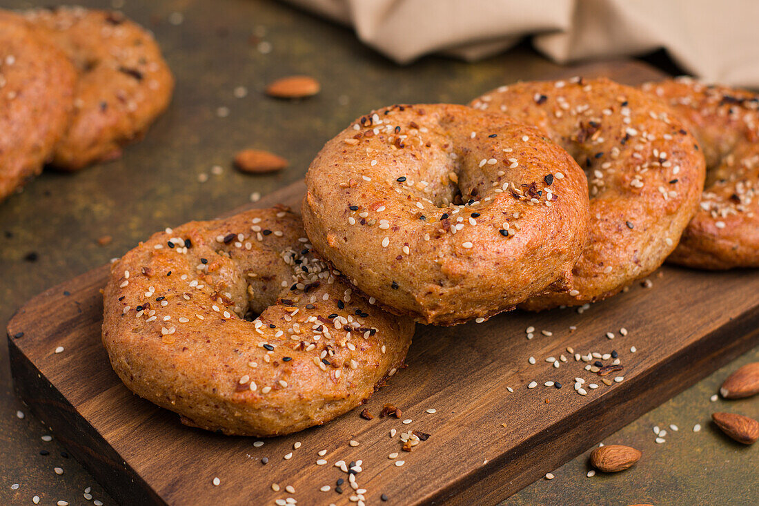 Leckere gebackene kohlenhydratarme Bagels auf einem hölzernen Schneidebrett auf einem Tisch mit Mandeln in einer hellen Küche