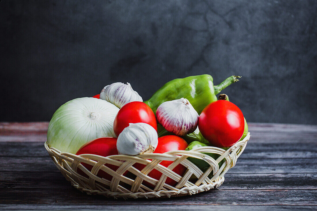 Frische reife Tomaten neben Paprika und Knoblauch in einer Schüssel auf einem Holztisch zu Hause