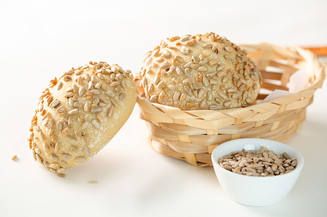 Frisch gebackene Brötchen mit Sonnenblumenkernen, serviert in einer Weidenschale auf weißem Hintergrund