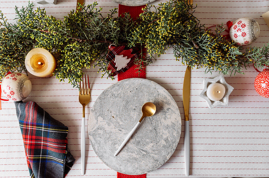 Von oben auf einen weihnachtlich gedeckten Tisch mit Kranzdekoration, rot und weiß, mit goldenem Besteck und Kerzen