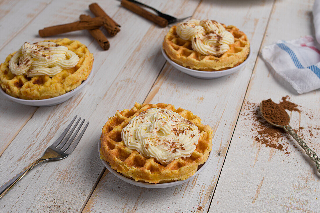 Von oben von frisch gebackenen hausgemachten Kürbis-Käse-Waffeln mit Zuckerguss auf Holztisch mit Zimtstangen in hellen Küche platziert