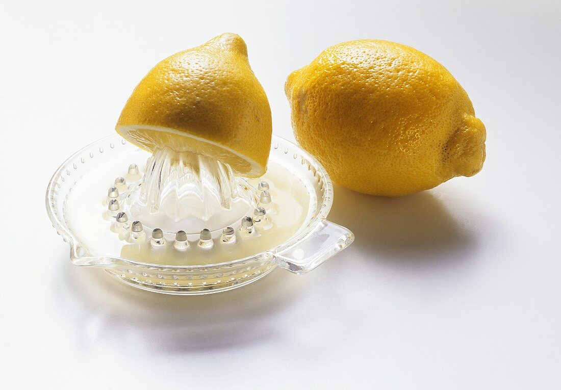 Zitronenhälfte auf Zitruspresse, dahinter ganze Zitrone
