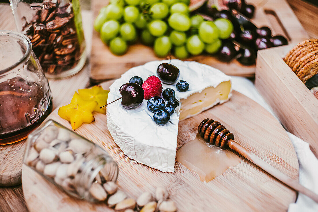 Frischer Camembert-Käse unter reifen Blaubeeren und Kirschen auf Holzbrett mit Honiglöffel