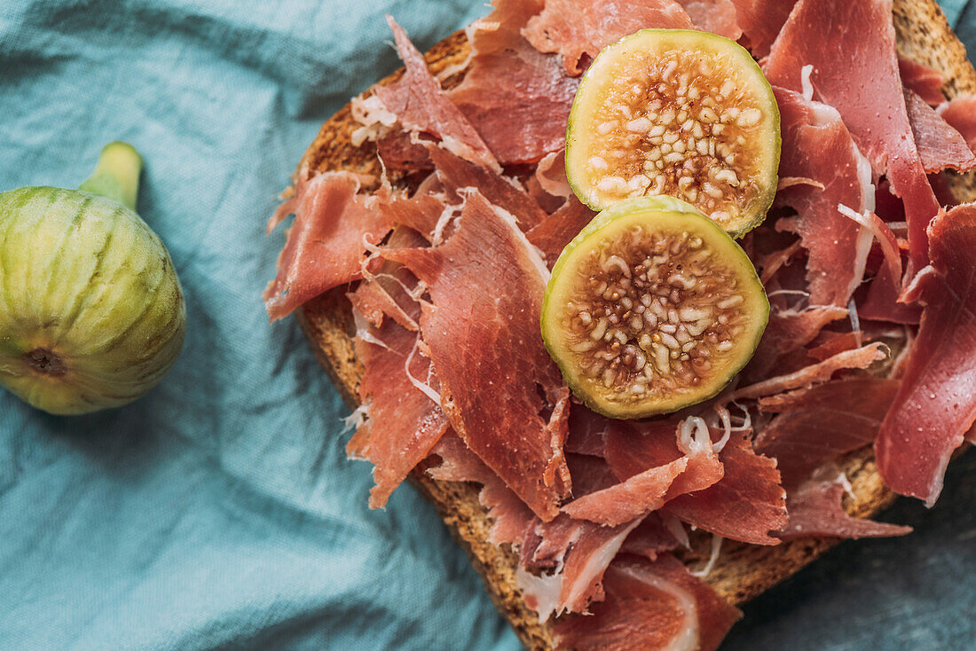 Köstlicher Toast mit Iberico-Schinken, Käse und frischen Feigen auf dem blauen Tischtuch, Köstliche Vorspeise, ideal als Aperitif. Gesundes Essen