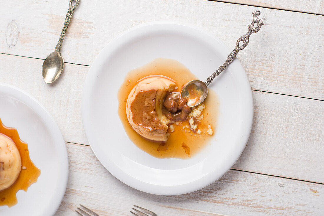 Draufsicht auf frischen Eierpudding mit süßer Dulce de Leche und Sirup auf einem Holztisch mit Besteck in der Küche