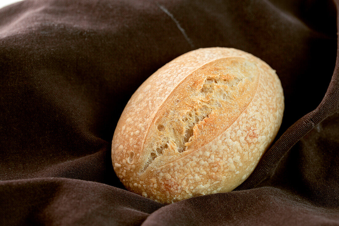 Blick von oben auf einen Laib leckeres frisches Brot auf braunem Stoff in einer Bäckerei