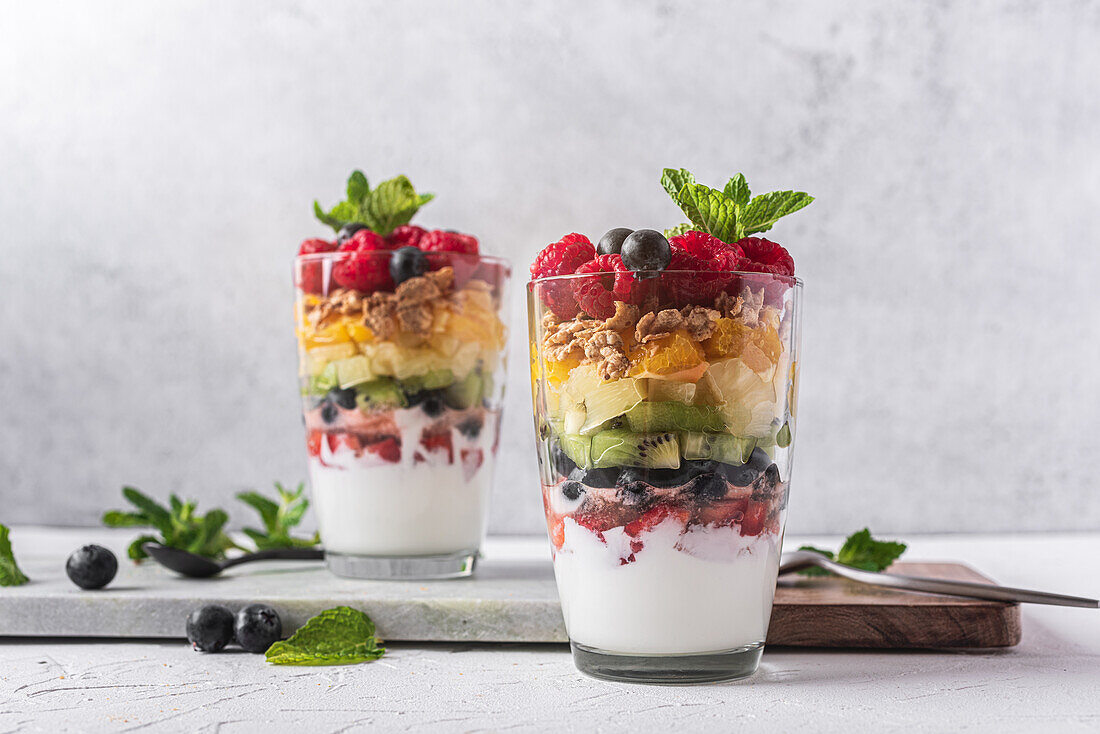 Appetitlicher Joghurt mit Schichten von frischen Früchten, serviert in Gläsern auf einem Tisch mit Minzblättern