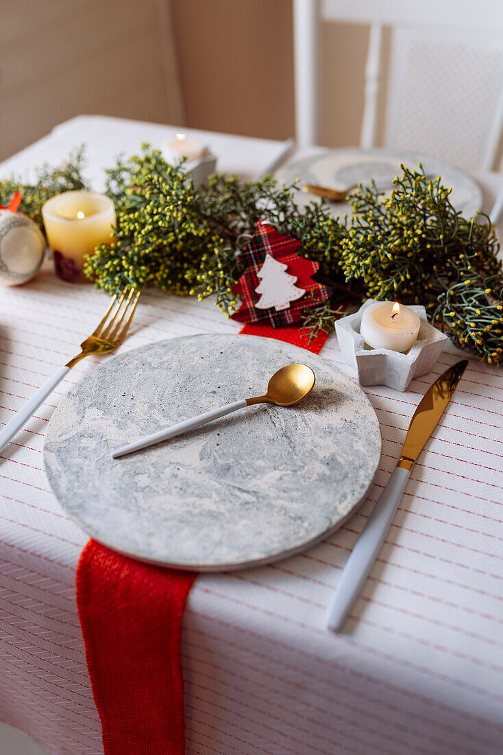 Von oben auf einen weihnachtlich gedeckten Tisch mit Kranzdekoration, rot und weiß, mit goldenem Besteck und Kerzen