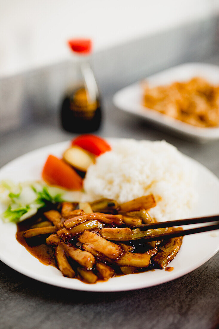 Appetitlich gekochte Yuxiang-Aubergine mit gesundem Gemüse und Reis auf weißem Teller in asiatischem Restaurant