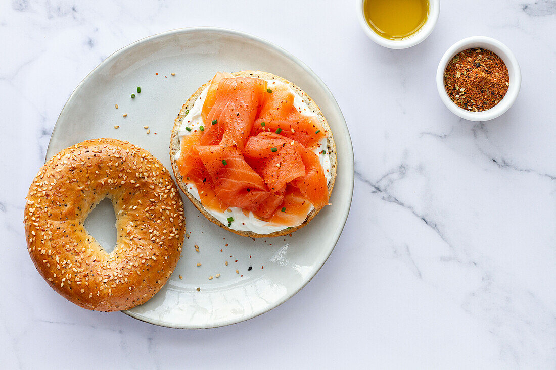 Von oben frischer Bagel mit Käse und Lachs auf einem Teller, serviert auf einem Tisch mit einer Tasse heißem Kaffee in einer hellen Küche