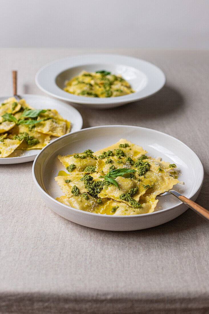 Appetitlich gekochte Ravioli Nudeln mit grüner Soße und Kräutern auf weißen Tellern mit Gabeln auf dem Tisch