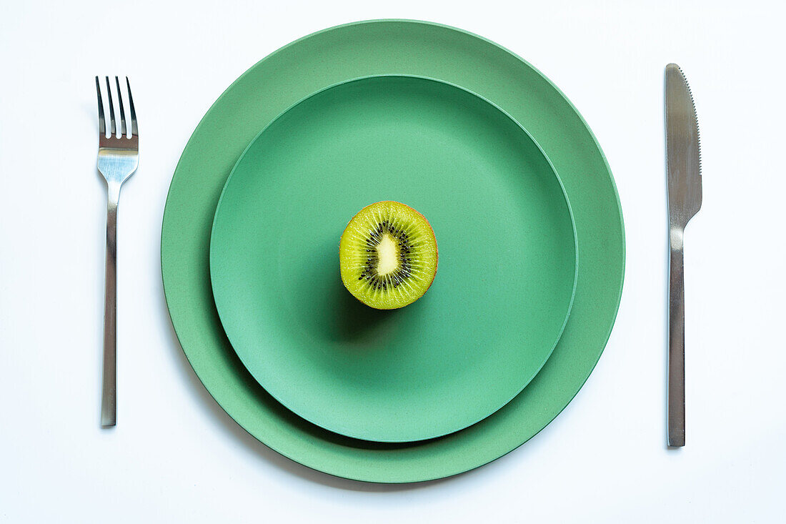 From above of half of fresh ripe juicy kiwi placed on green ceramic plates on white surface