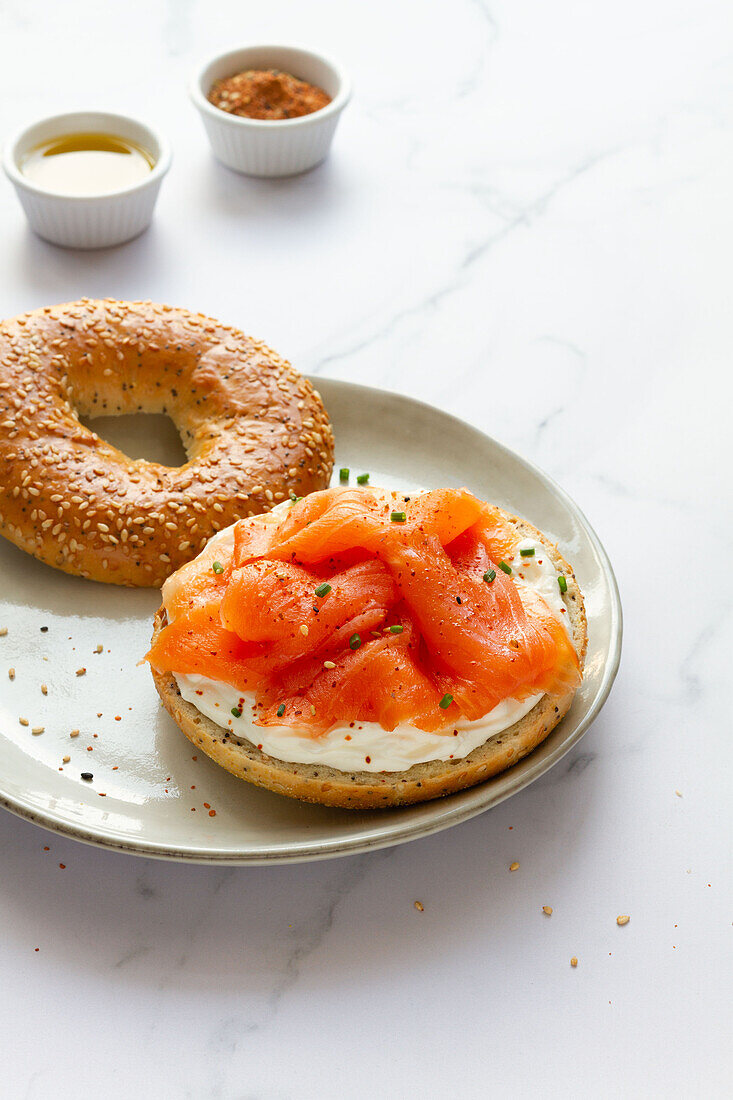 Frischer Bagel mit Käse und Lachs auf einem Teller, serviert auf einem Tisch mit einer Tasse heißem Kaffee in einer hellen Küche