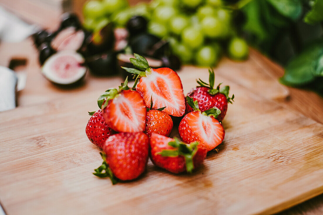 Reife köstliche Erdbeeren vor Feigen und Weintrauben auf einem Holzbrett auf dem Tisch