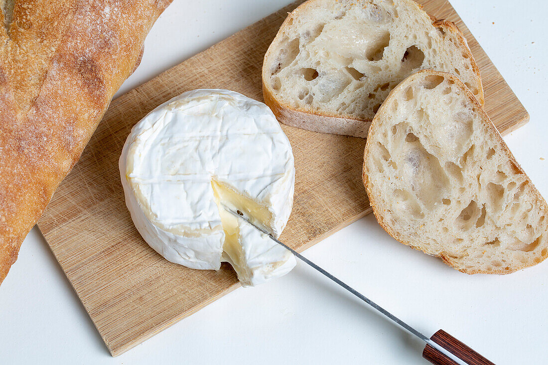 Von oben köstlicher Camembert-Käse auf hölzernem Schneidebrett neben Brotscheiben auf weißem Hintergrund